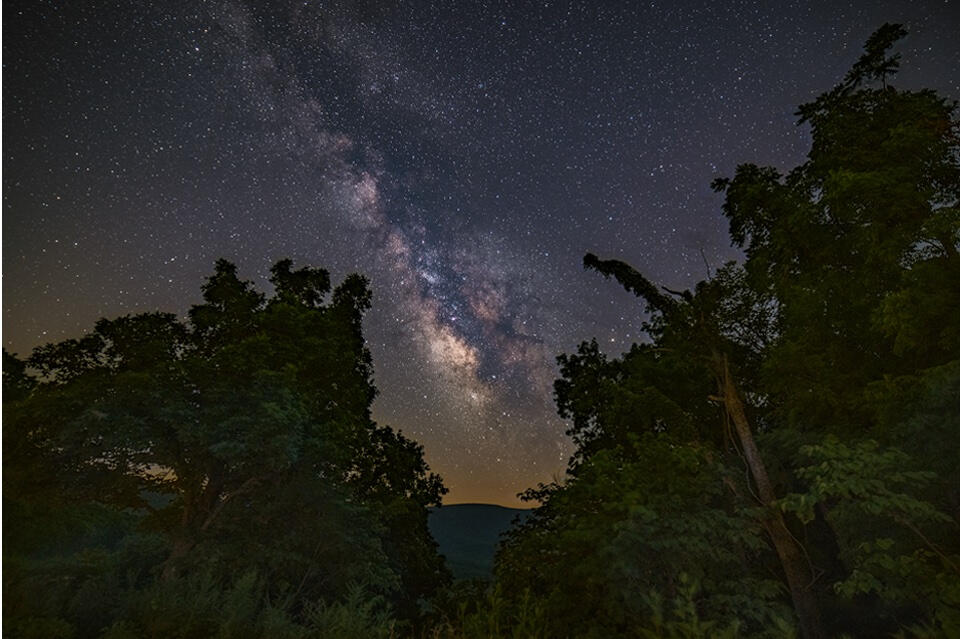 A personal landscape astrophotography shot featuring the Milky Way galaxy arching over a dark terrestrial horizon, showcasing the blend of earth and sky in Shenandoah National Park.